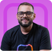 Um homem de óculos sentado em frente a um fundo roxo.